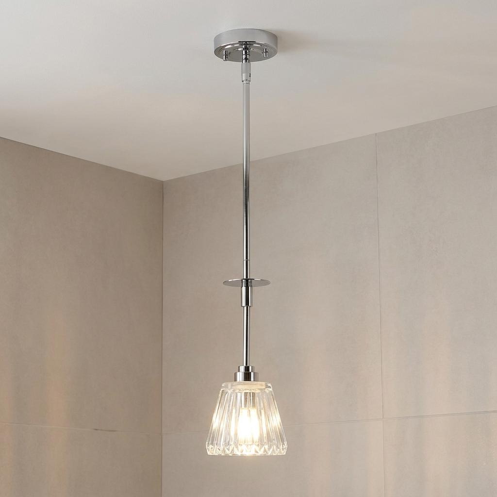Polished chrome pendant bathroom light with a ribbed glass shade hanging against a tiled wall.