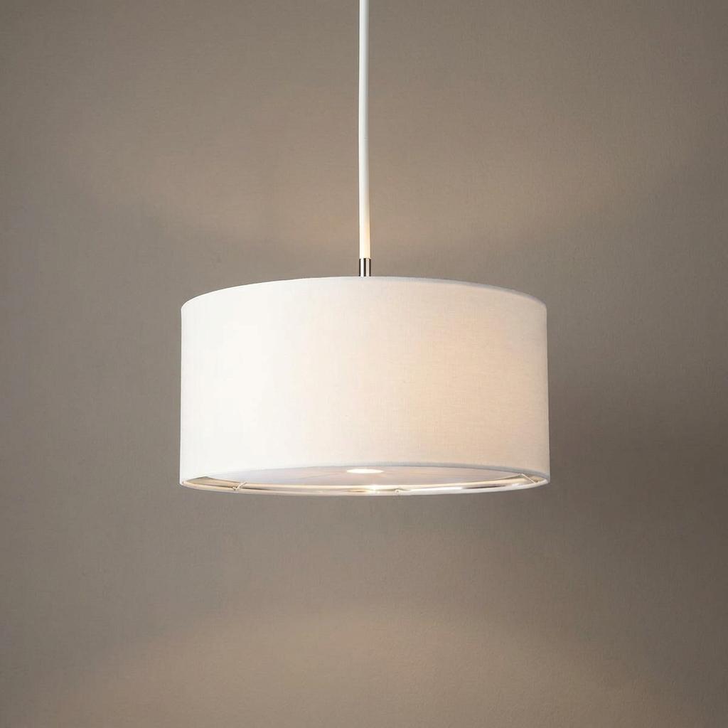 A white fabric drum pendant light with polished nickel accents, glowing against a neutral backdrop.