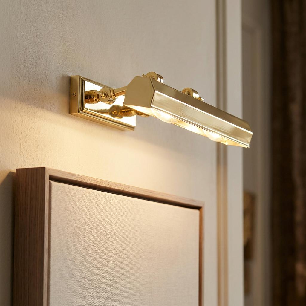 Medium polished brass picture light mounted on a wall above a framed artwork, emitting a warm glow.