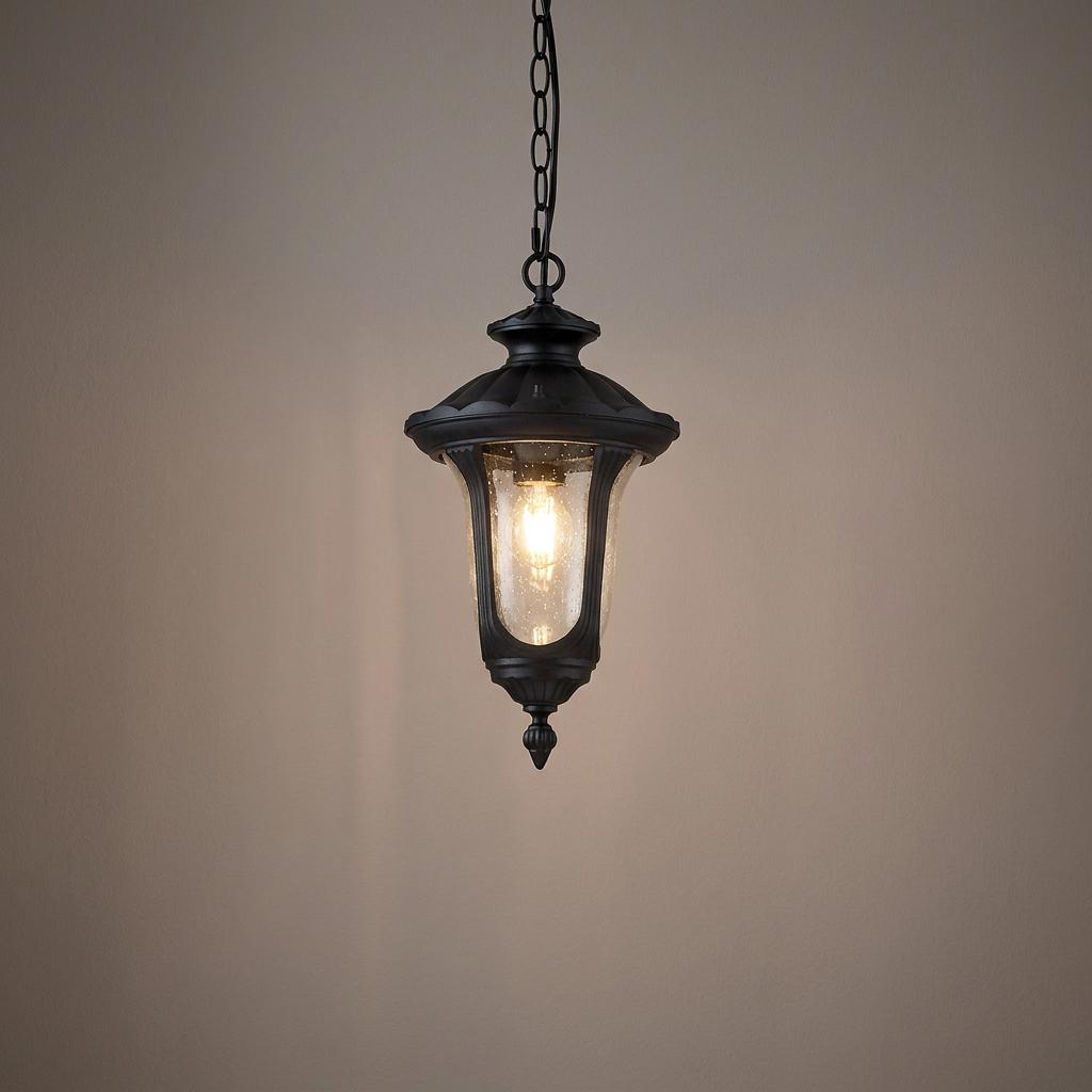 Black hanging outdoor lantern with seeded glass and a glowing bulb against a neutral background.