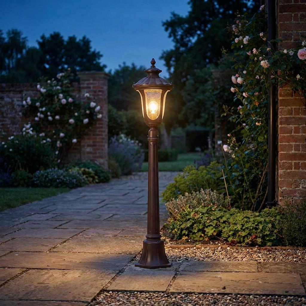 Traditional bronze bollard light with seeded glass glows on a stone garden path at dusk.