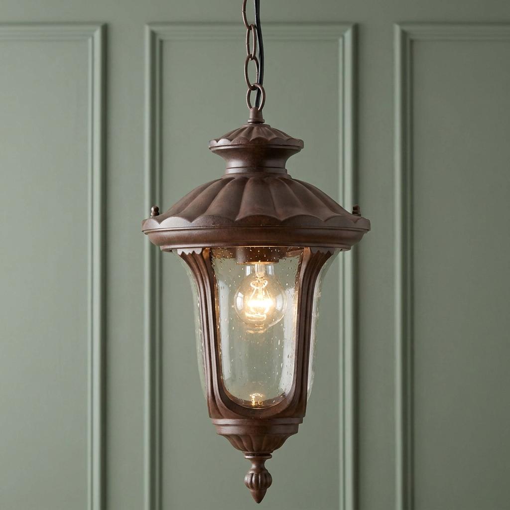 Traditional rusty bronze outdoor lantern with a seeded glass shade and glowing bulb against a green paneled wall.