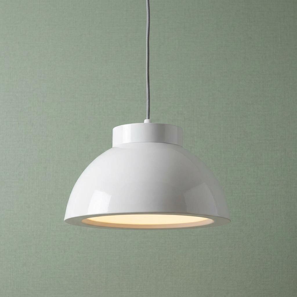 Glossy white dome LED pendant light emitting warm light against a textured green background.