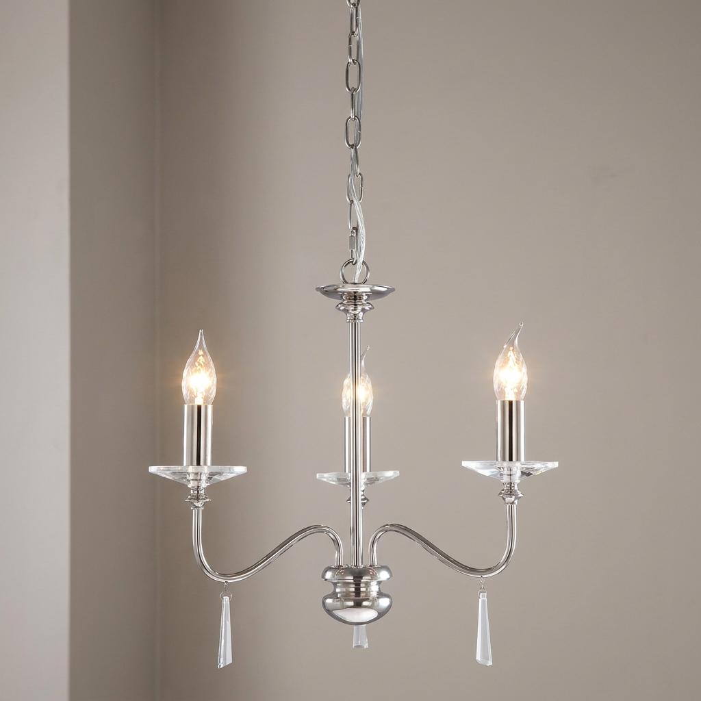 Polished nickel 3-light chandelier featuring glass accents and lit candle bulbs against a neutral wall.