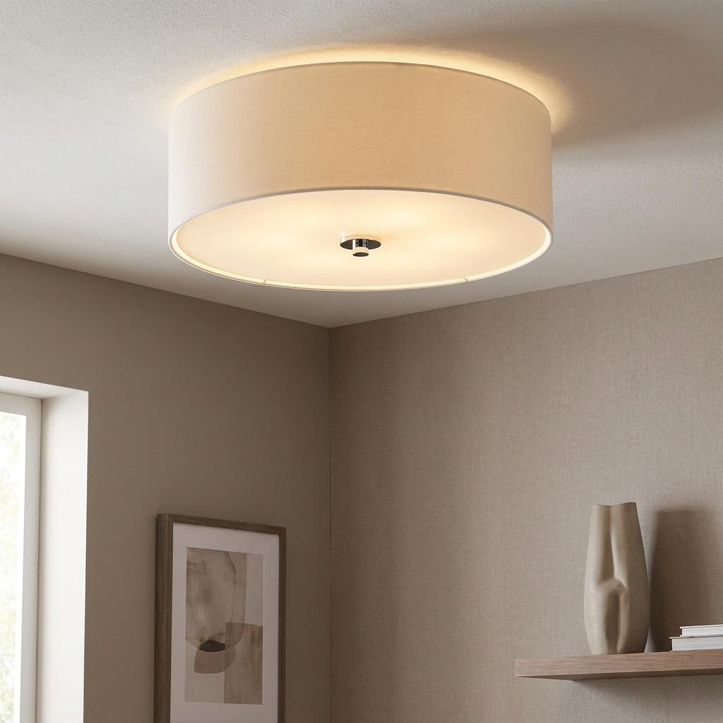 A warm-glowing cream drum ceiling light with a chrome finial in a contemporary living room setting.