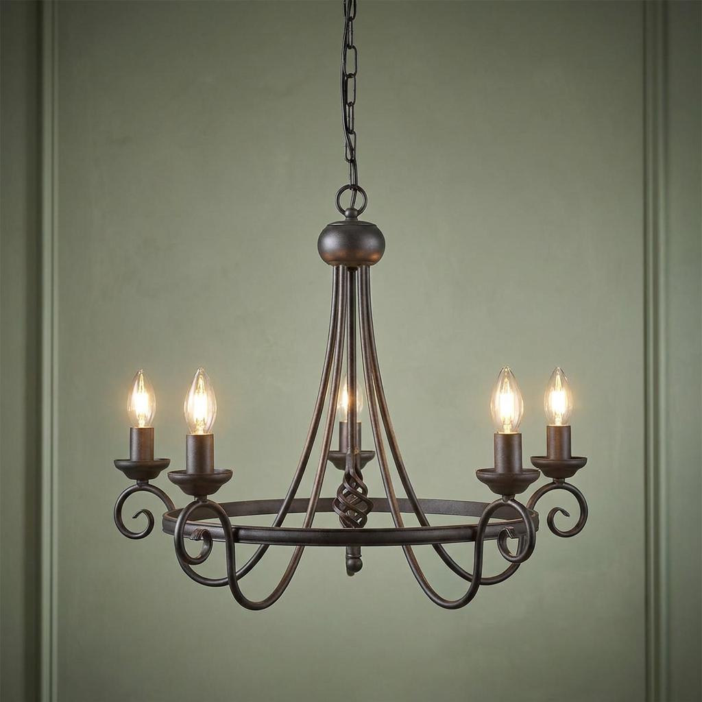 Elstead Harlech 5-light black chandelier with scrolled metal arms and glowing candle bulbs against a green wall.