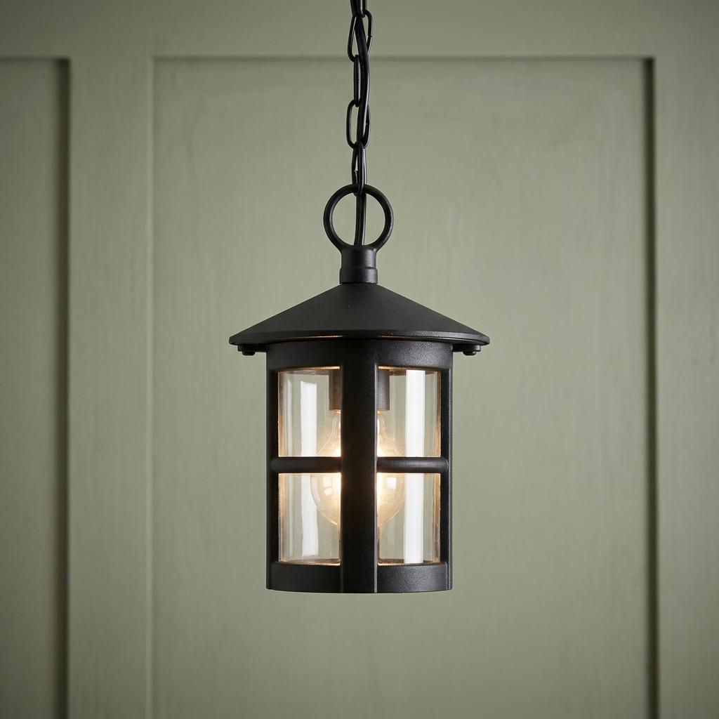 Black lantern-style outdoor pendant light with clear glass panels hanging against a pale green paneled wall.