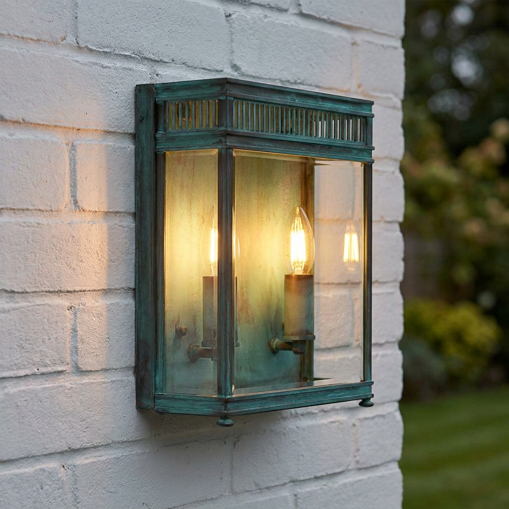 Elstead Holborn verdigris outdoor wall lantern with two lit candle bulbs mounted on a white brick wall.
