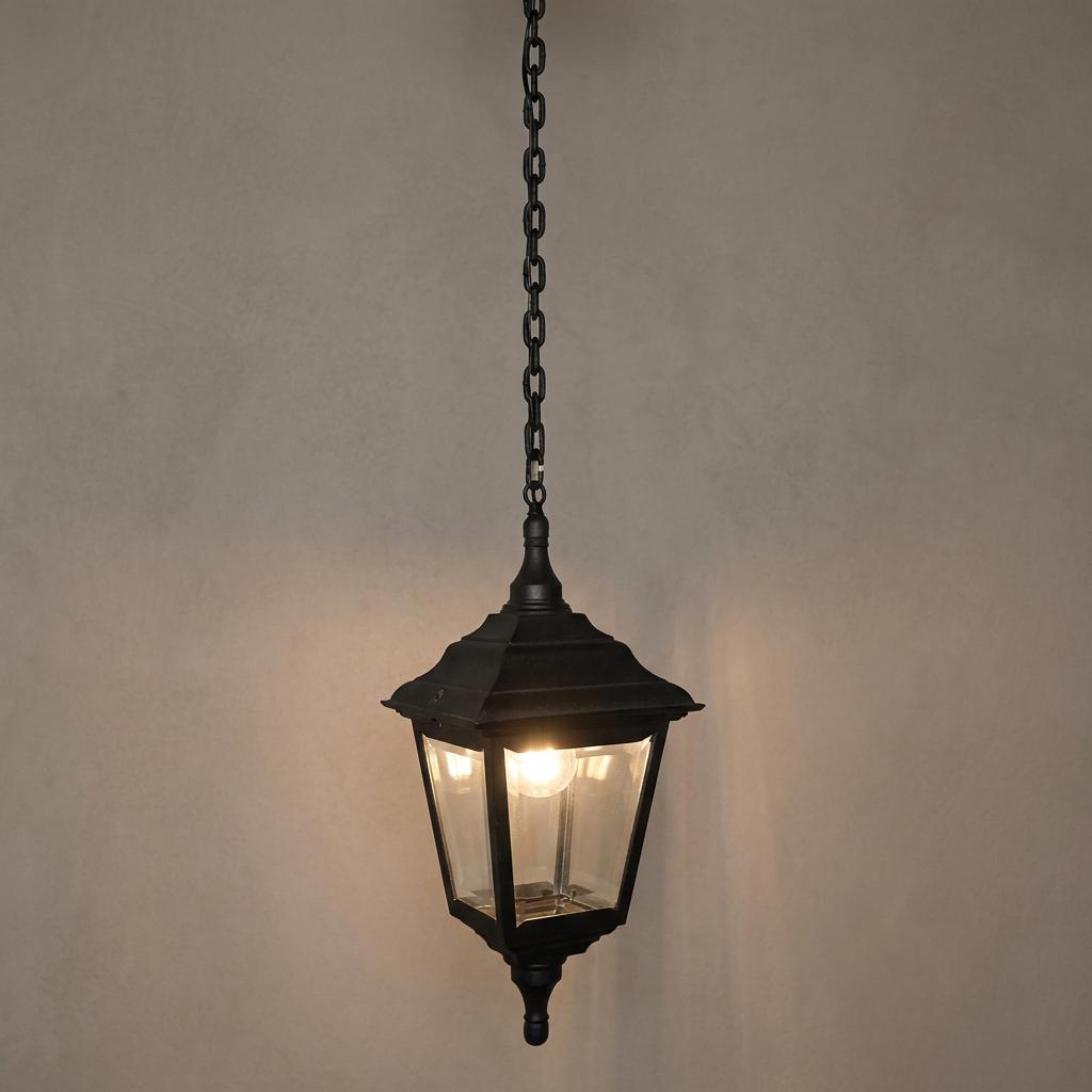 Traditional black outdoor pendant lantern with clear glass panels and a glowing bulb, hanging from a metal chain.