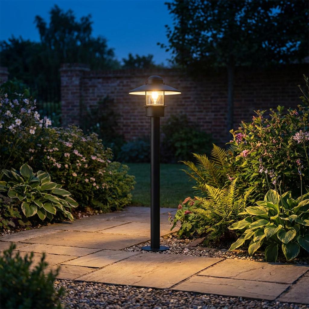 A black Elstead Klampenborg bollard light illuminates a stone garden path at twilight.