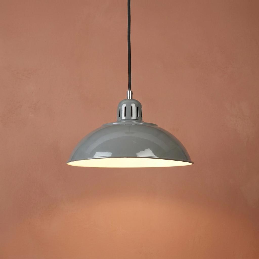 Grey industrial-style dome pendant light with a white interior glowing against a textured terracotta wall.