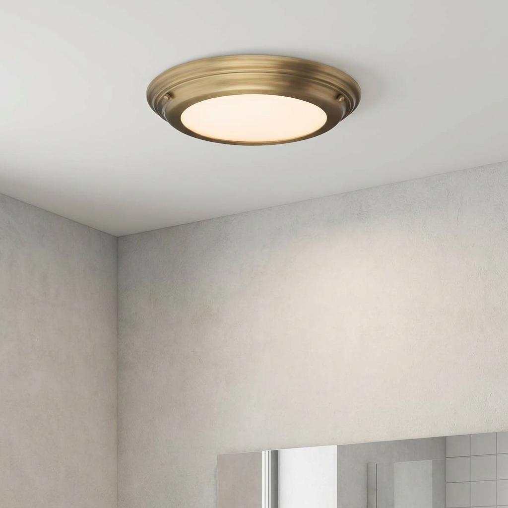 Welland flush mount bathroom ceiling light in aged brass with frosted opal glass on a white ceiling.