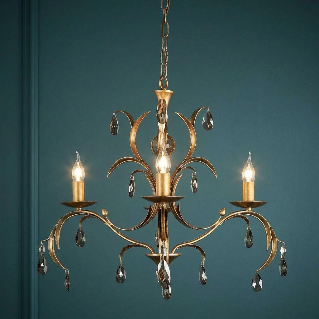 Elstead Lily 3 light antique bronze chandelier with crystal droplets lit against a dark teal wall.