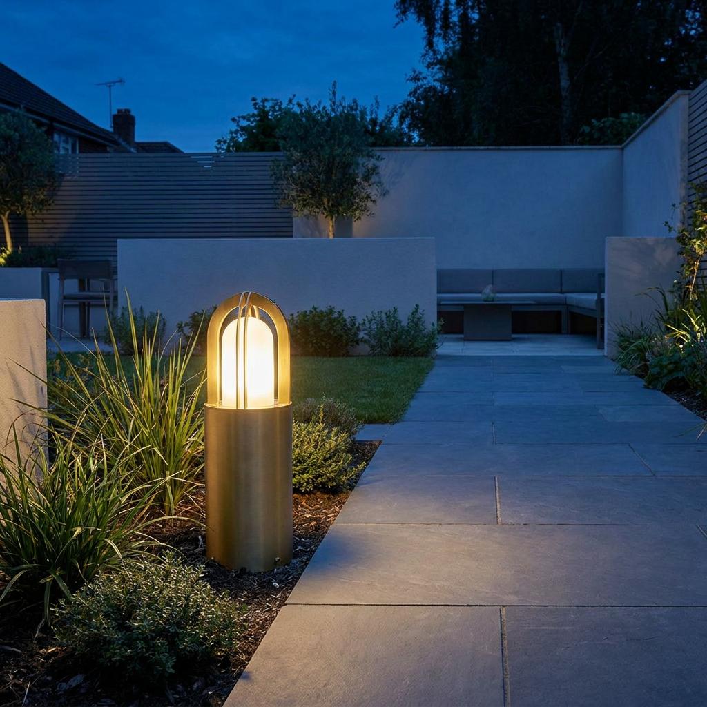 Elstead Paignton brass bollard light illuminating a modern stone garden path at twilight.