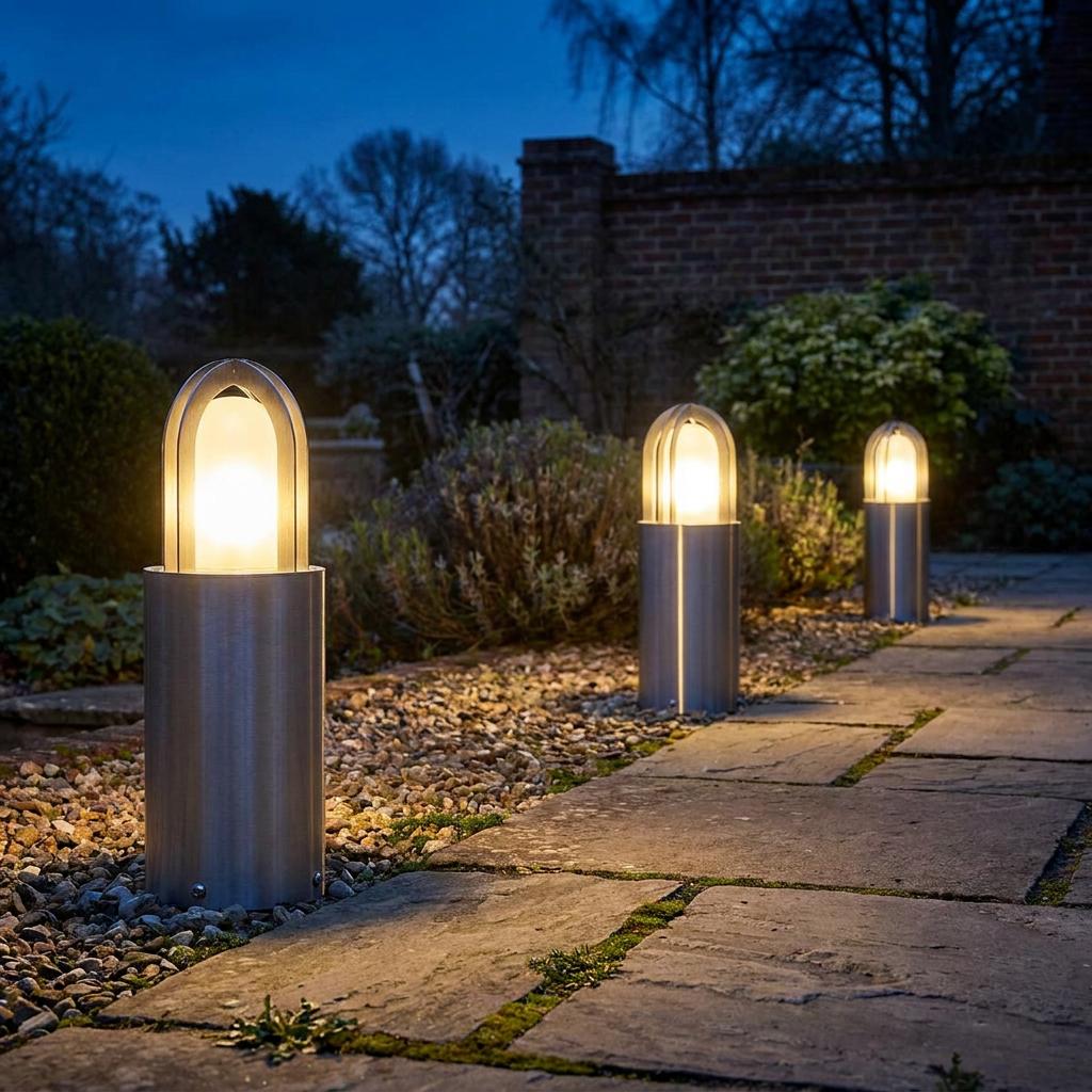 Three silver bollard lights illuminating a stone garden path with a warm glow at night.