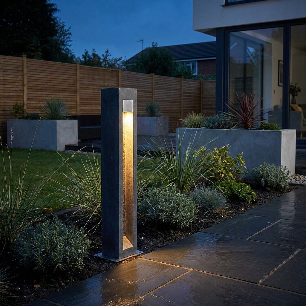 An Elstead Parkstone LED bollard with a warm glow illuminates a slate patio path in a landscaped garden at dusk.