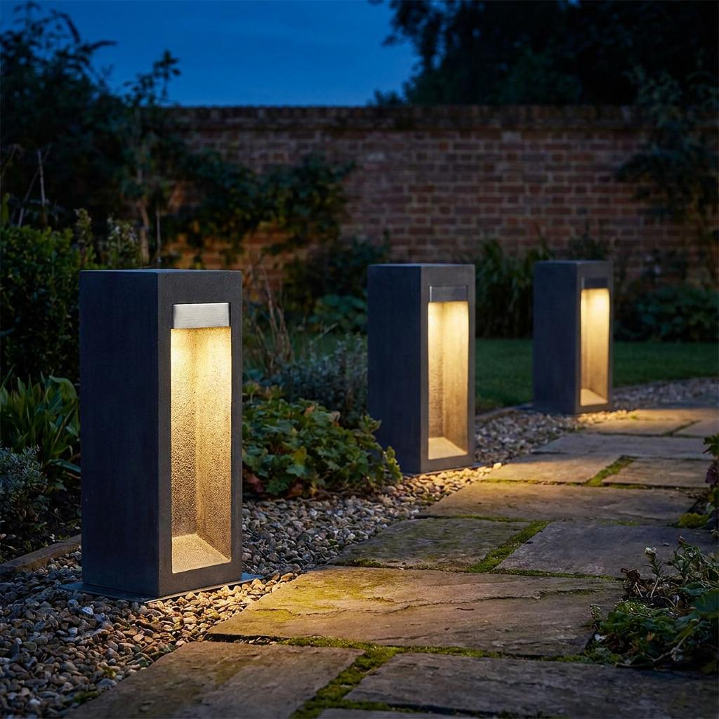 Three modern grey rectangular bollard lights illuminating a stone garden path at dusk.