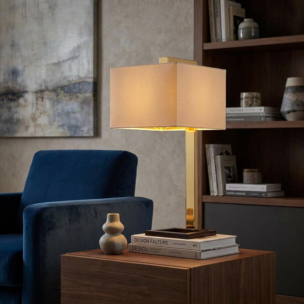 Polished gold table lamp with a rectangular cream shade on a side table beside a blue velvet armchair.