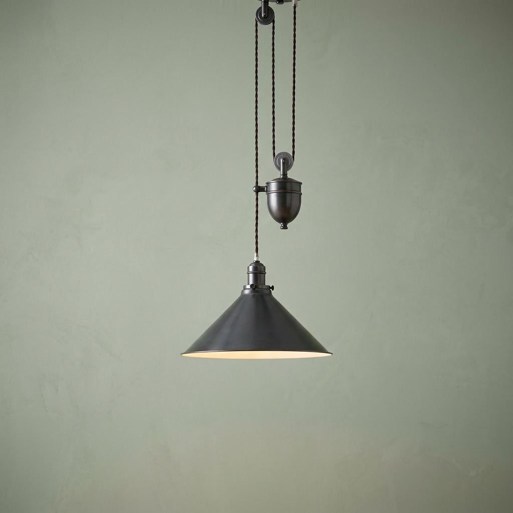 Old bronze rise and fall pendant light with a conical shade and pulley system against a sage green wall.