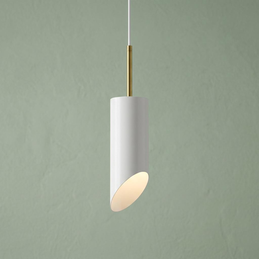 White cylinder pendant light with an angled base and brass stem, glowing against a sage green background.