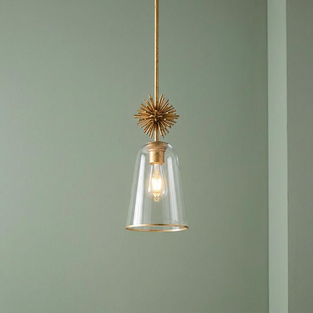 Gold starburst pendant light with a clear glass shade hanging against a muted green wall.