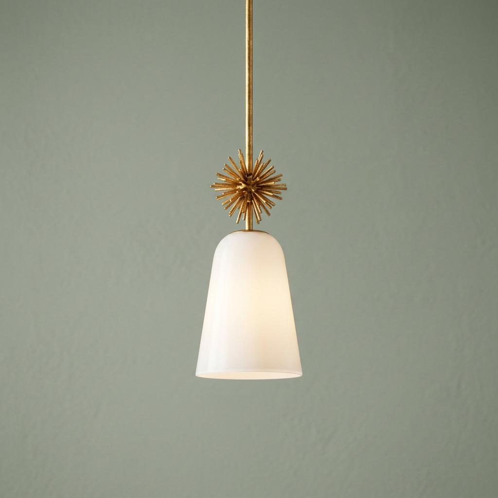 Gold pendant light with a spiky starburst accent and a bell-shaped opal glass shade against a green wall.