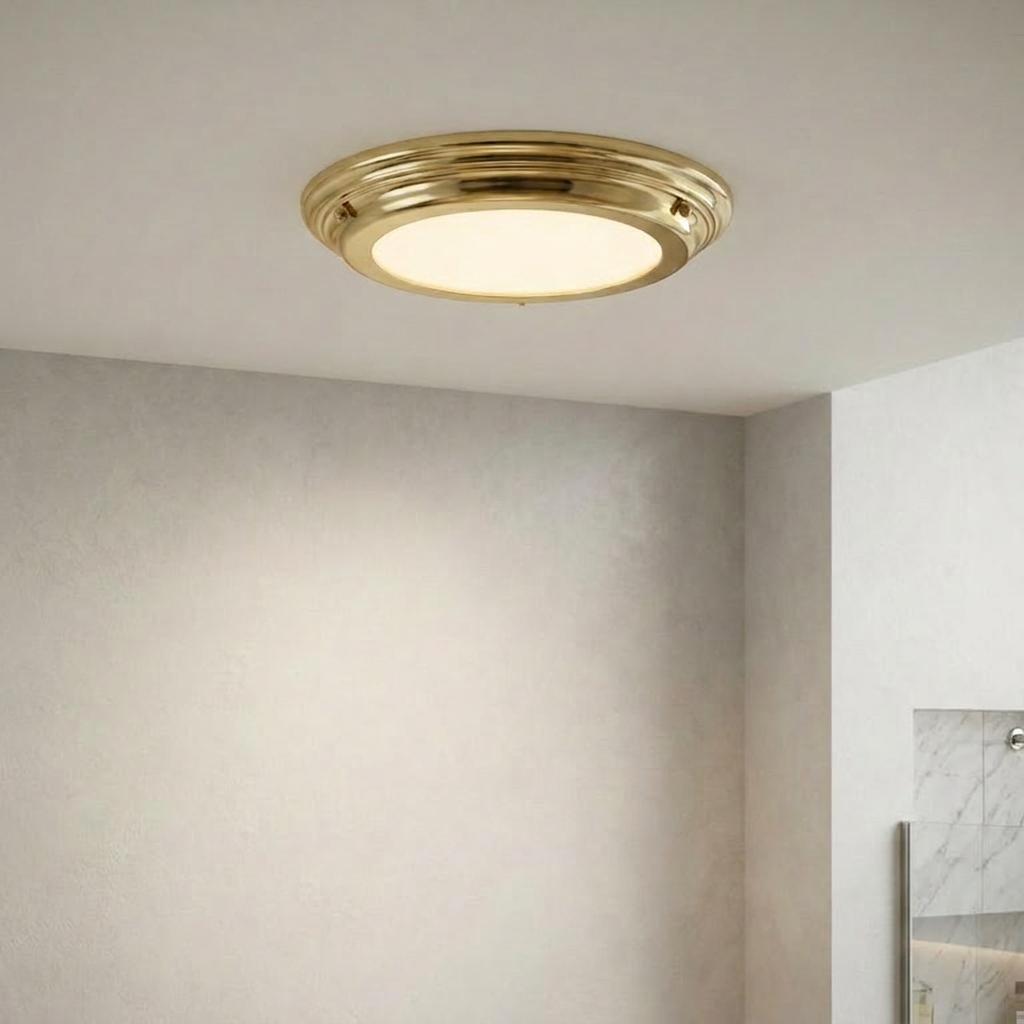Round Elstead Welland flush bathroom ceiling light with a polished brass frame and white opal glass diffuser.
