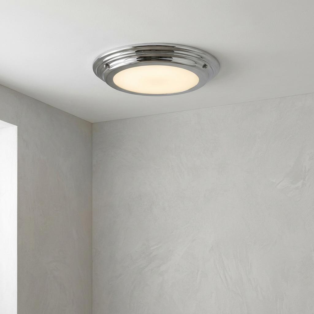 A polished chrome flush ceiling light with an opal glass diffuser glowing warmly on a white ceiling.