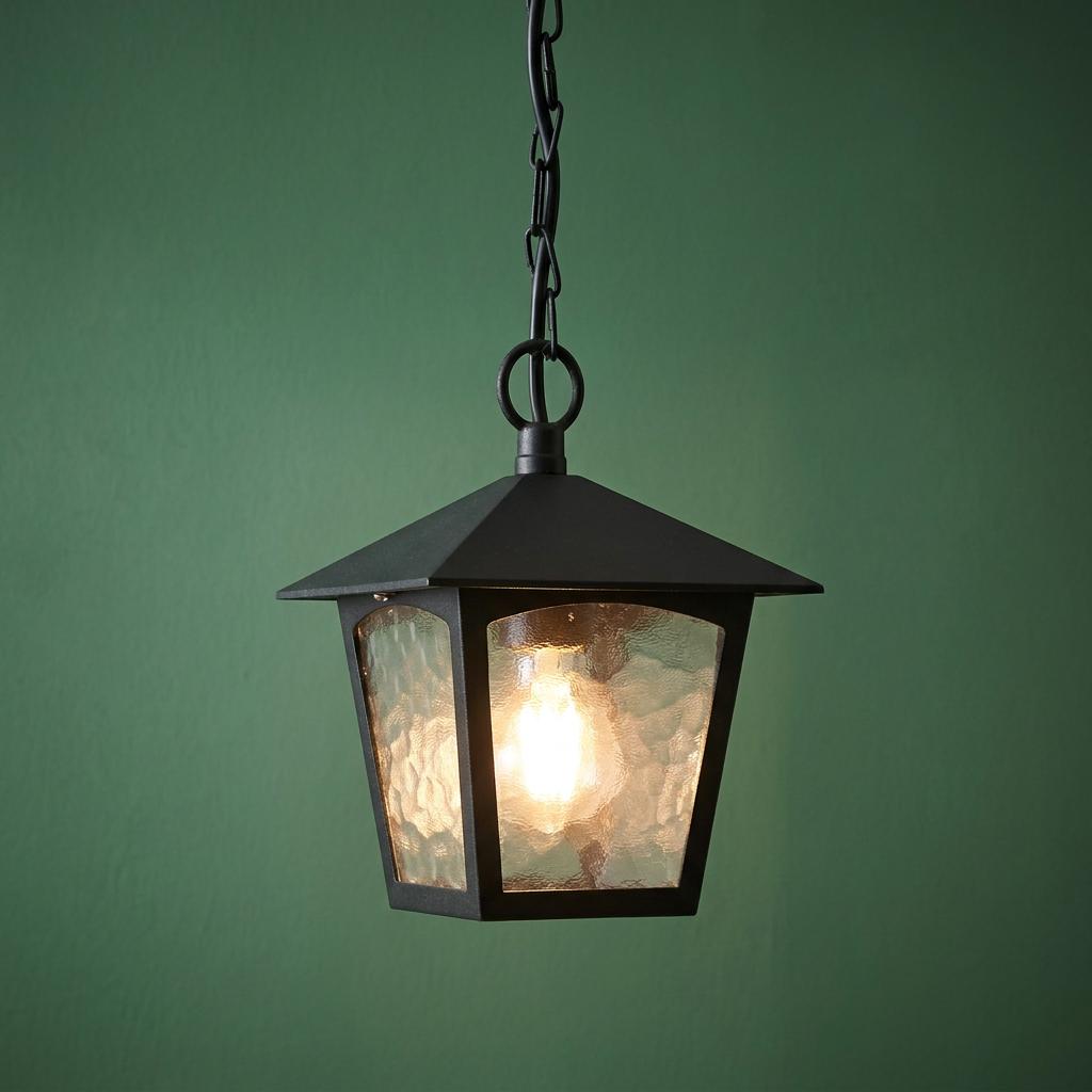Traditional black outdoor pendant lantern with textured glass panels hanging from a chain against a green wall.