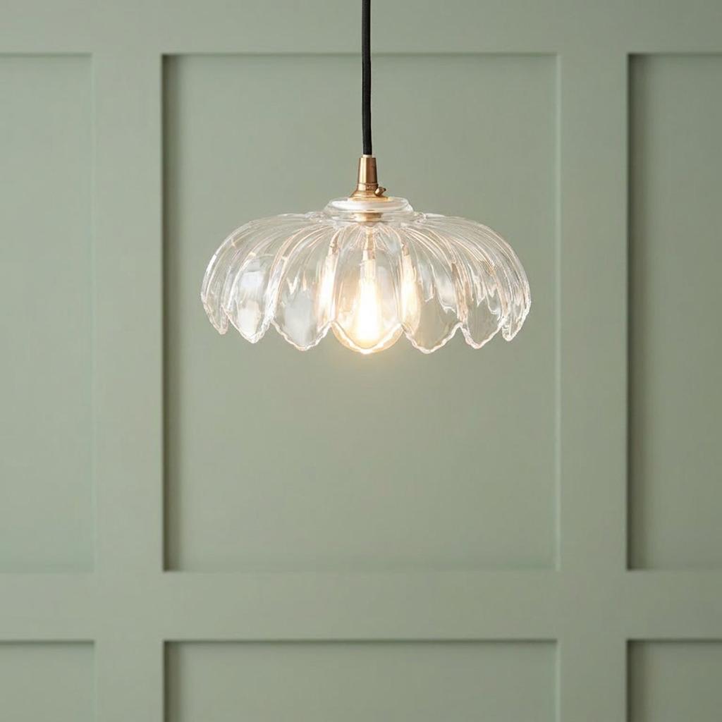 Scalloped clear glass pendant light with a brass fitting and black cable against a sage green paneled wall.
