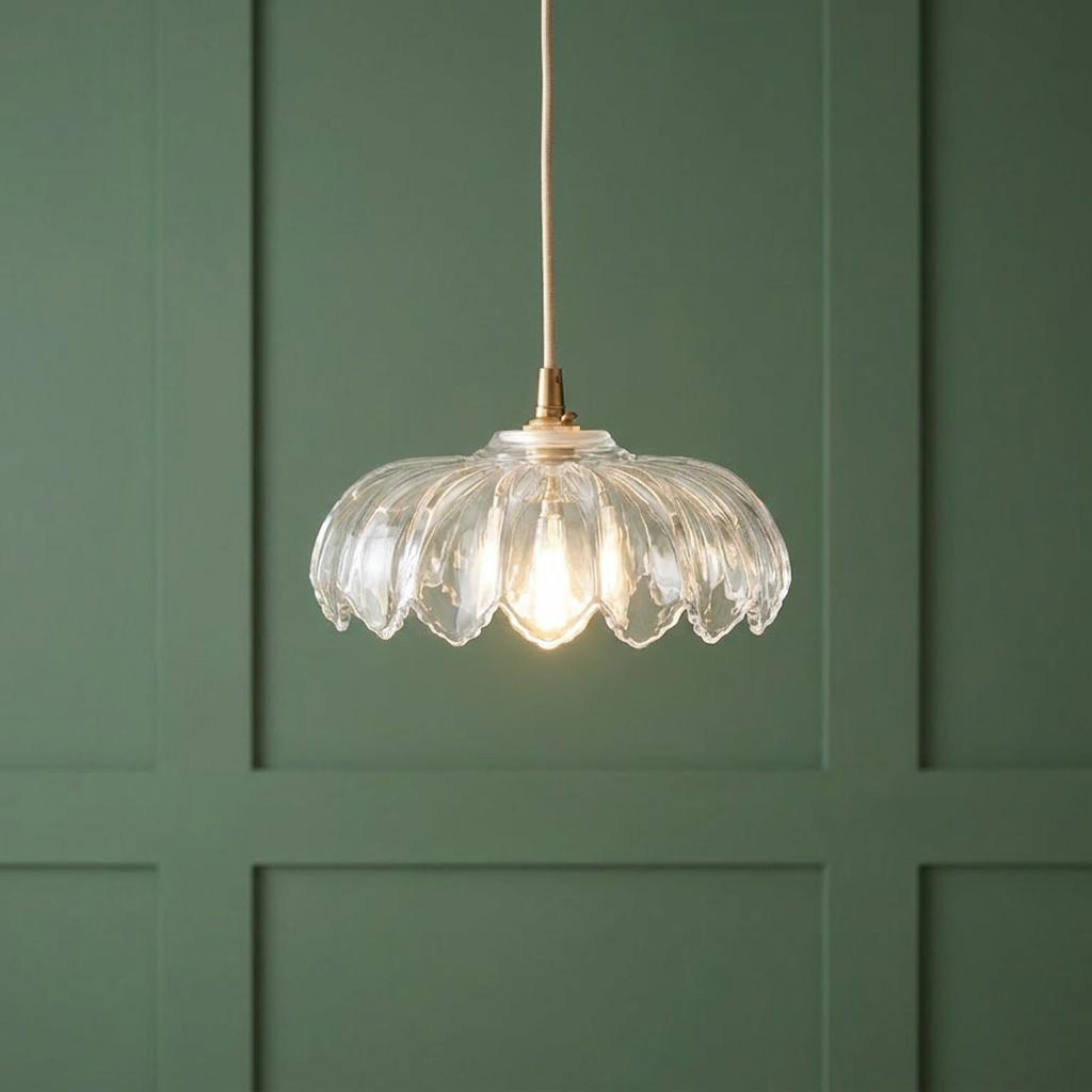 Scalloped glass pendant light with brass hardware lit against a green paneled wall.