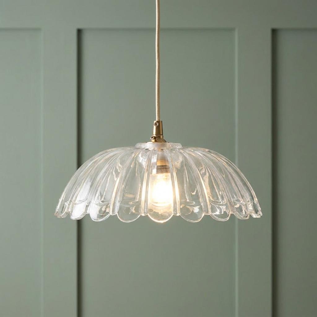 Scalloped clear glass pendant light with brass fixture and natural cord hanging against a green paneled wall.
