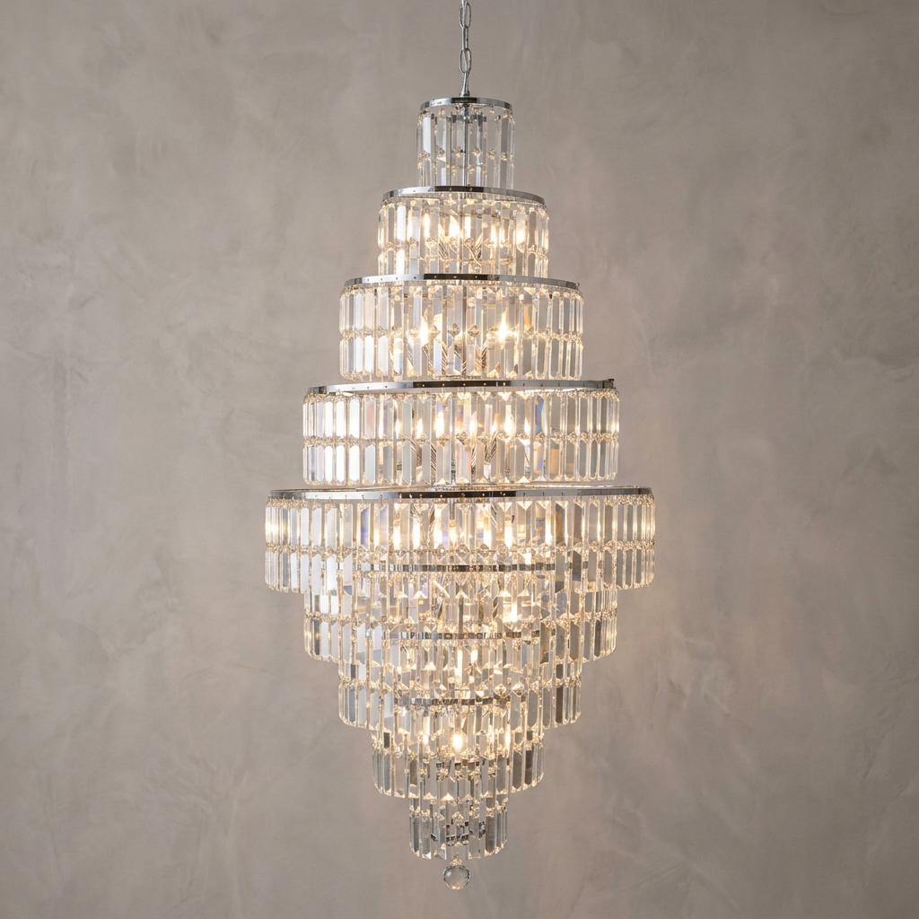 Large tiered chandelier with polished chrome finish and rectangular crystal prisms hanging against a neutral wall.
