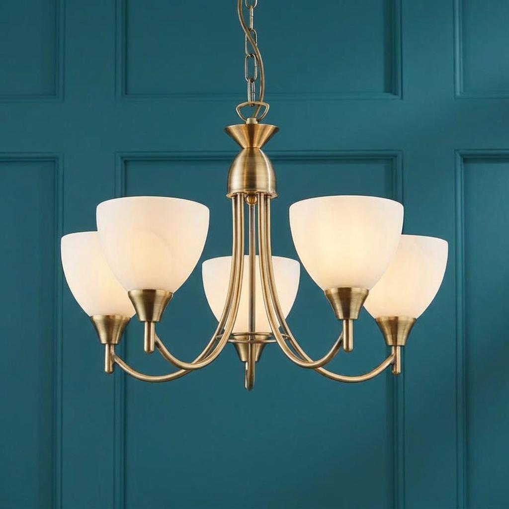 Endon Alton 5 arm antique brass ceiling pendant with white glass shades against a teal paneled wall.