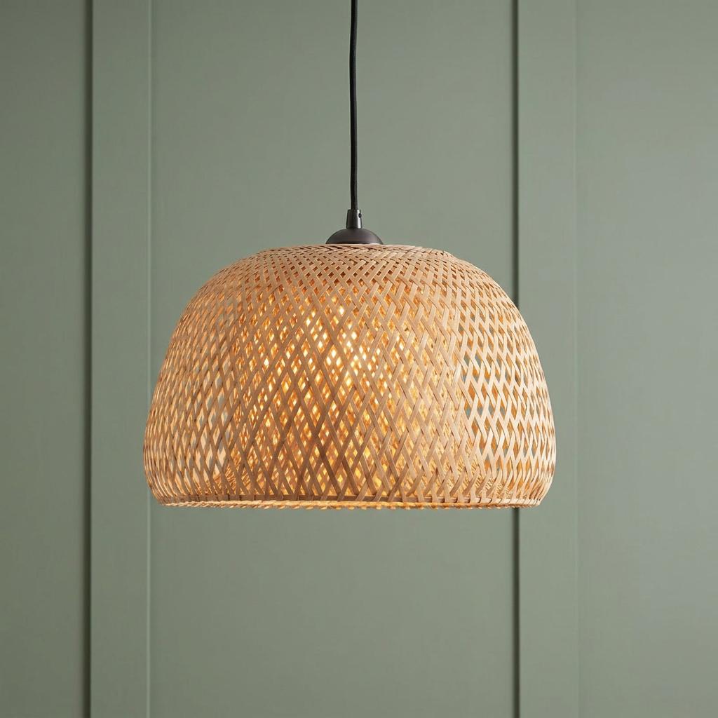Woven bamboo dome pendant light glowing warmly against a sage green paneled background.