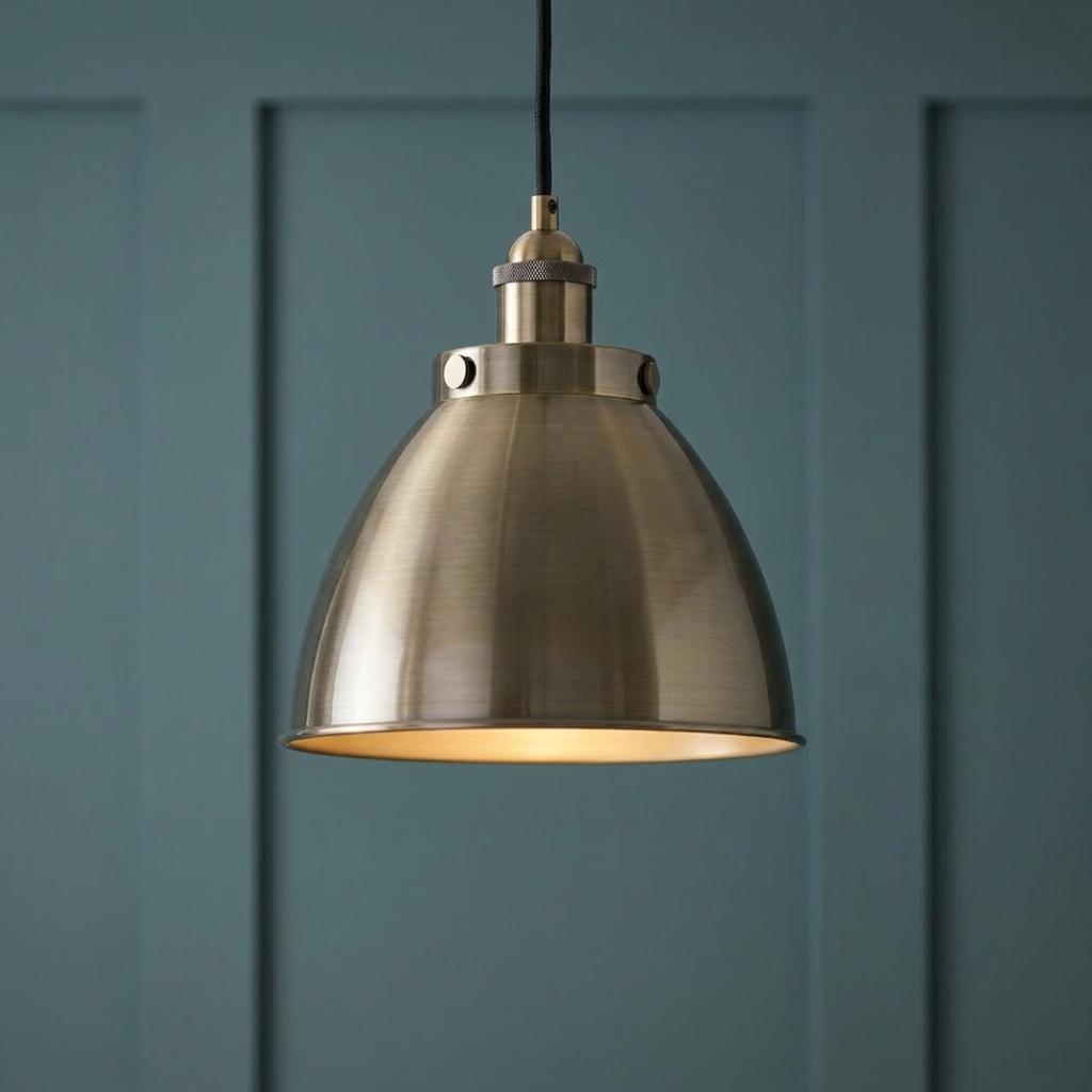 Antique brass industrial dome pendant light hanging against a dark teal paneled wall.