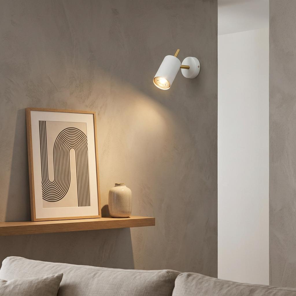 White and satin brass LED spotlight mounted on a grey wall above a wooden shelf with a framed picture.