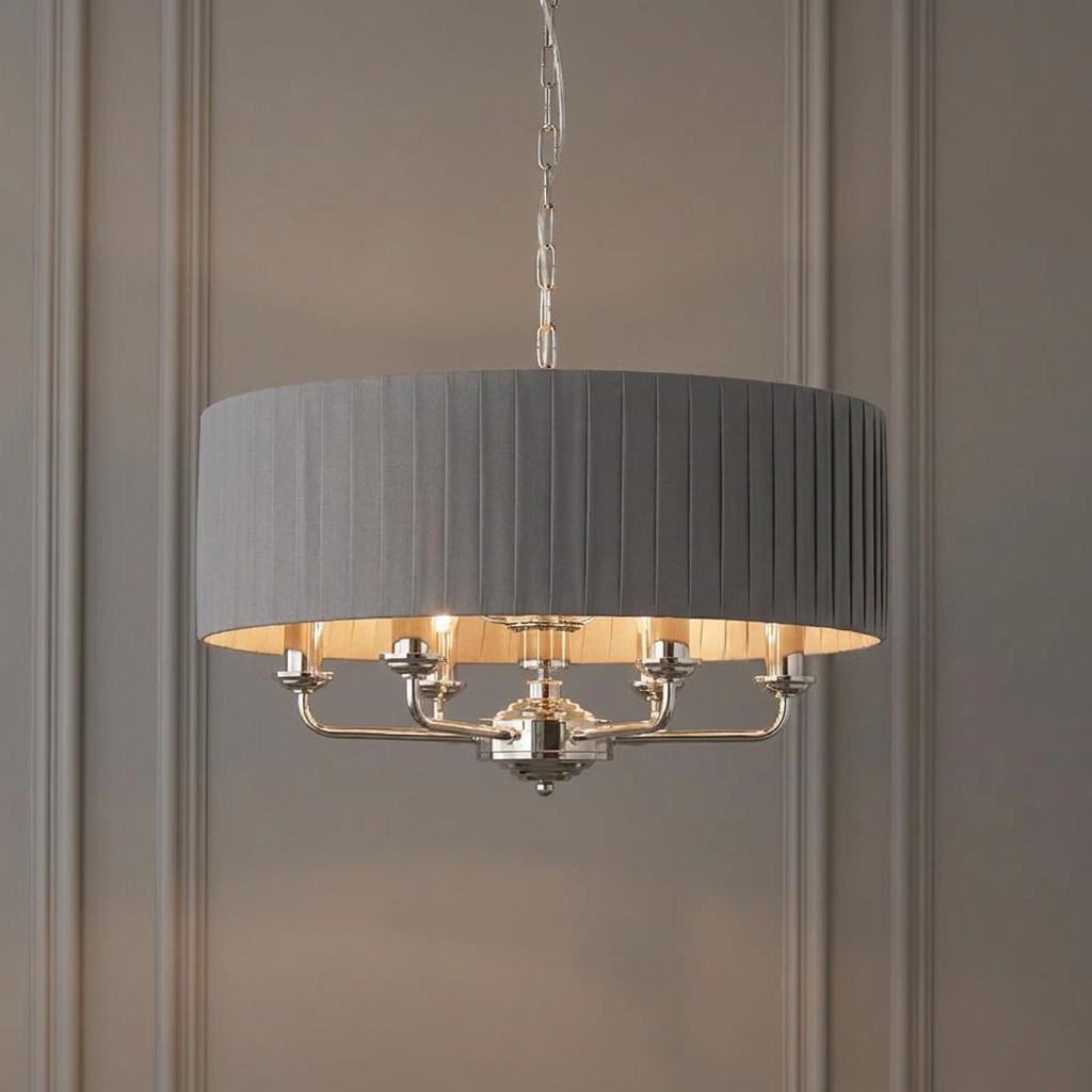 Six-light bright nickel pendant chandelier with a charcoal pleated drum shade, hung against a paneled wall.