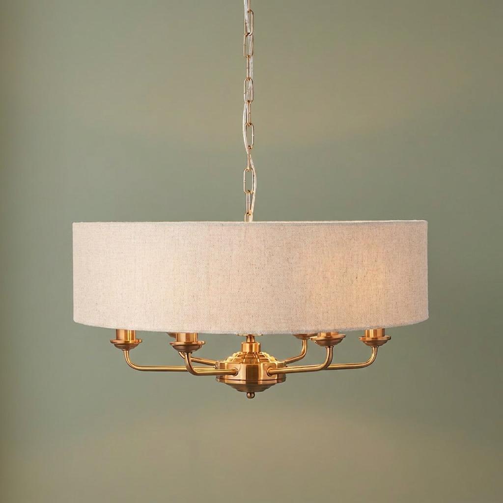 Vintage brass 6-light pendant chandelier with a wide oatmeal linen drum shade against a plain green background.