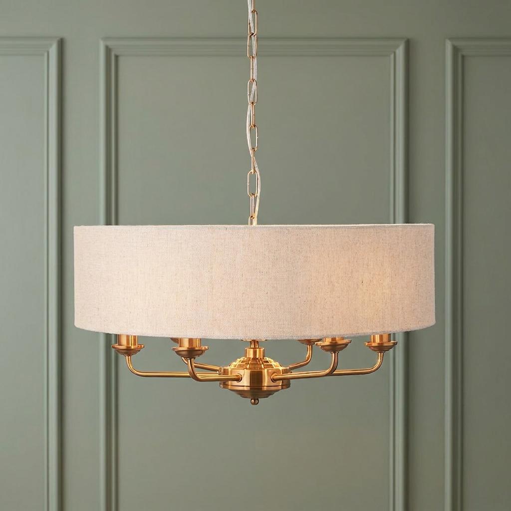 Vintage brass 6-light pendant with a linen drum shade hanging against a sage green paneled wall.