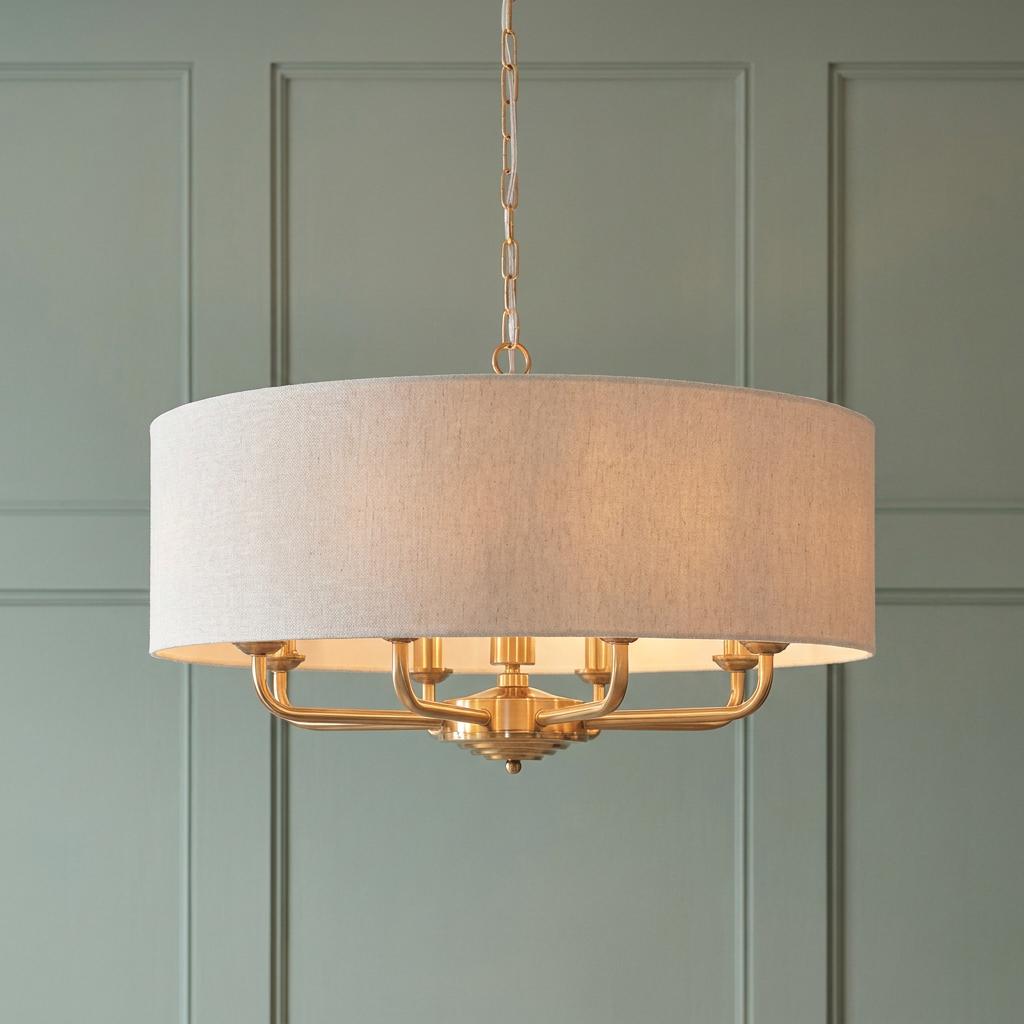 Vintage brass 8-light pendant with a grey linen drum shade against a green paneled wall.