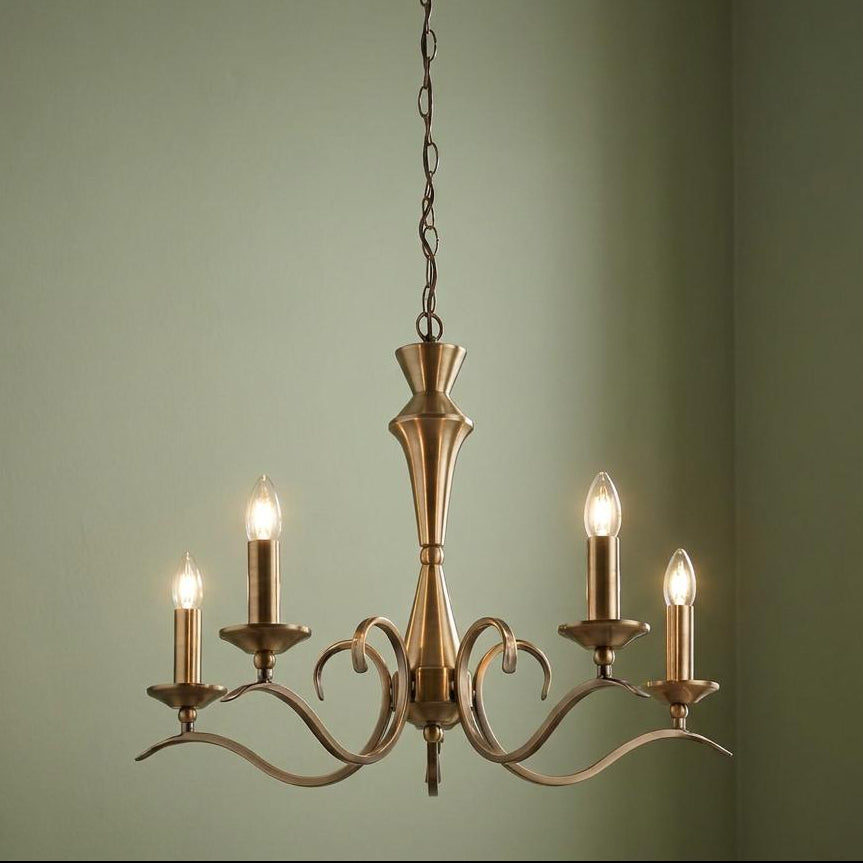 Endon Kora antique brass 5-light chandelier with curved arms and glowing candle bulbs against a sage wall.