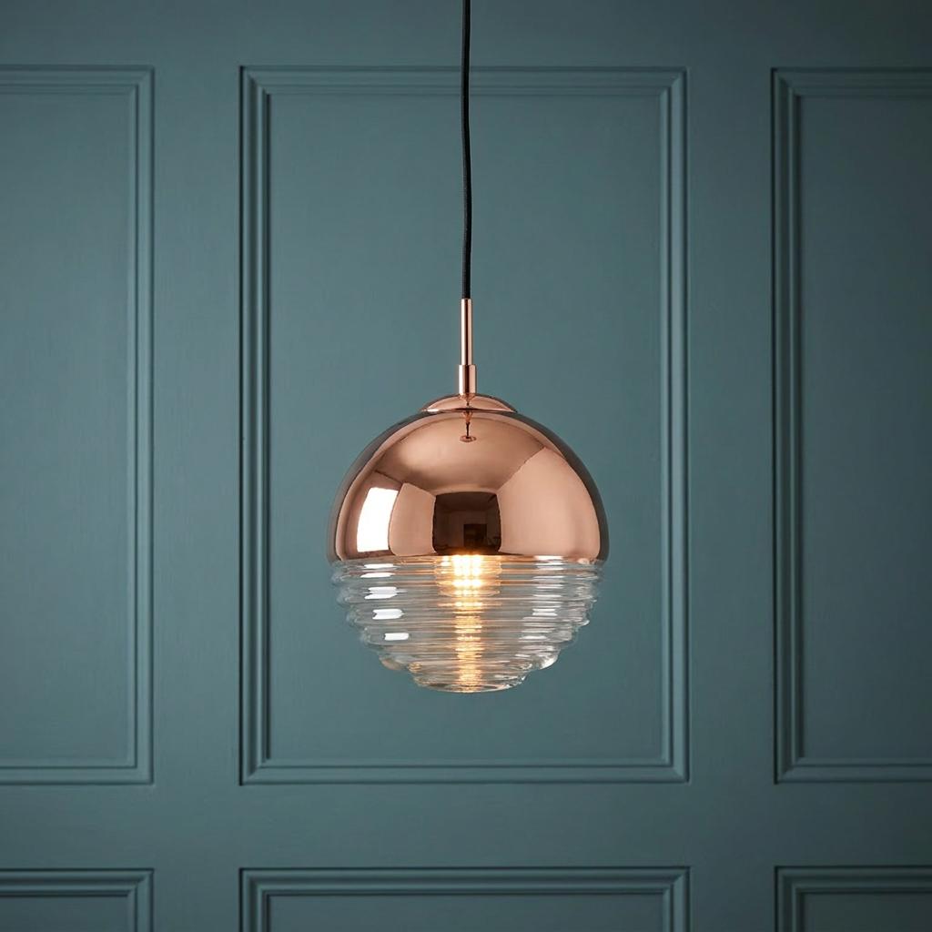 A copper and ribbed glass globe pendant light glows against a teal paneled wall.