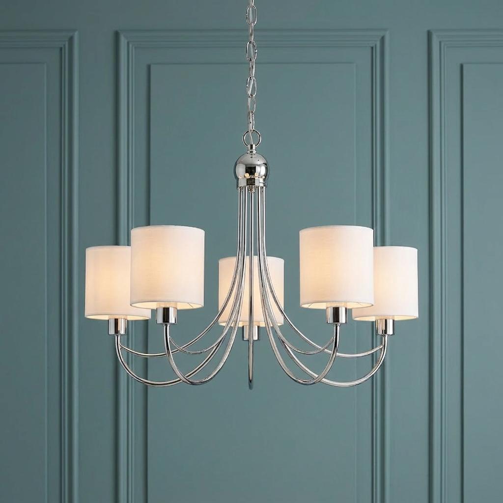 Chrome five-arm chandelier with white cylinder shades against a teal paneled wall.