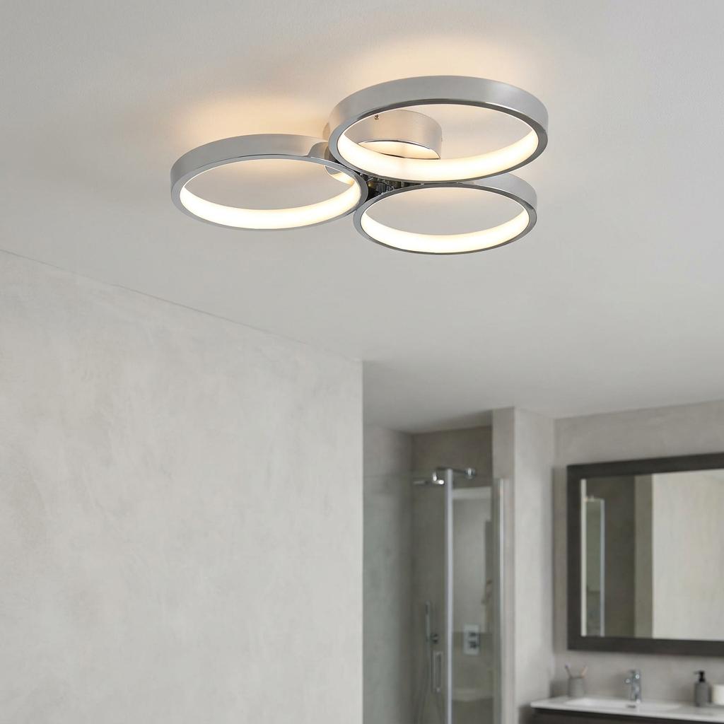 Modern chrome semi-flush ceiling light with three glowing LED rings installed in a contemporary bathroom.