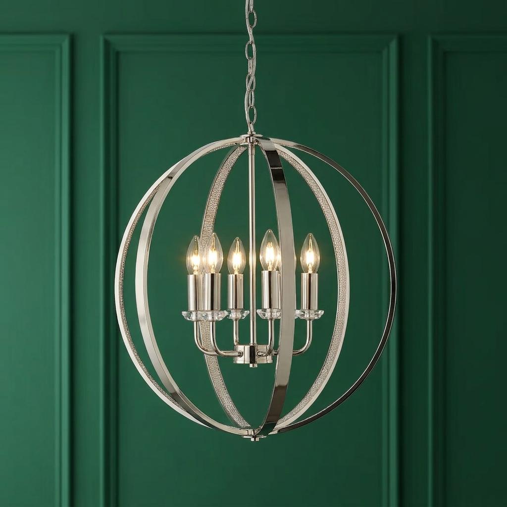 Polished nickel orbital globe pendant light with six candle bulbs set against a green paneled wall.