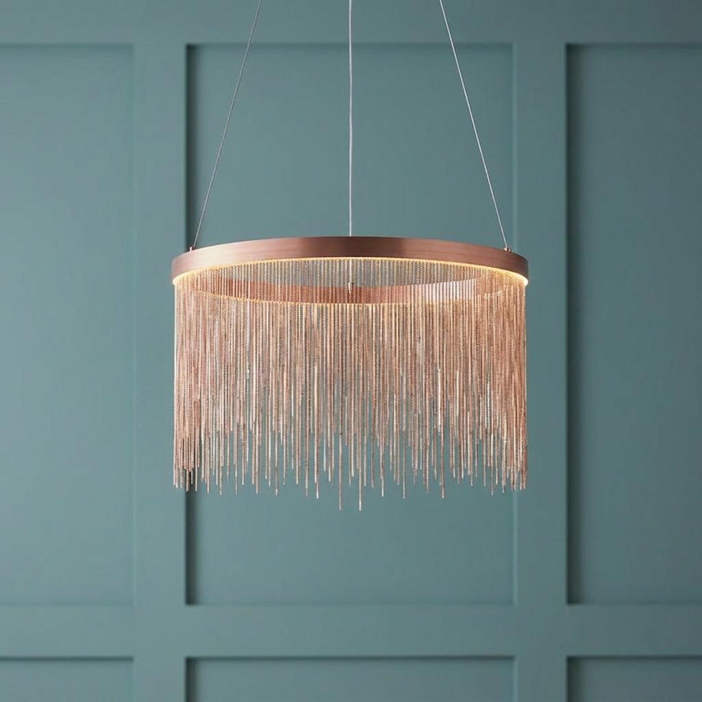 Modern circular copper pendant light with a delicate chain fringe against a teal paneled wall.