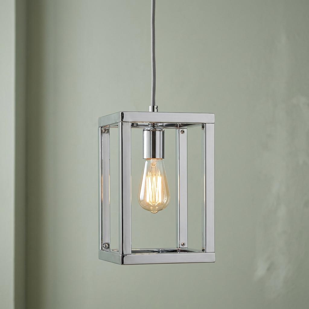 Polished nickel lantern pendant light with a filament bulb suspended against a pale green wall.