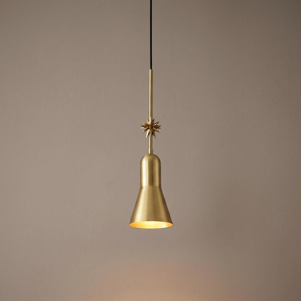 Aged brass pendant light with a conical shade and a gold starburst ornament against a neutral background.