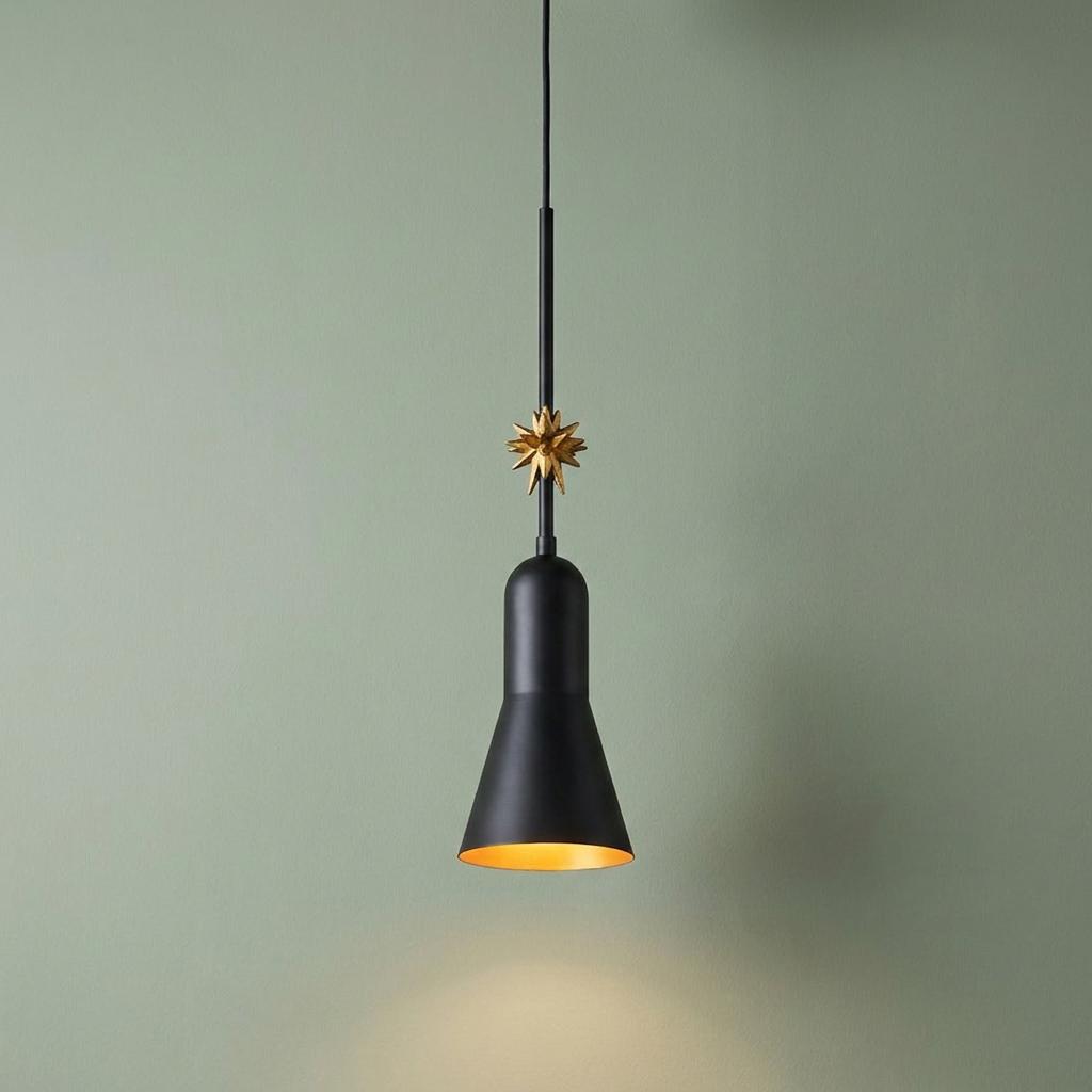 Matte black conical pendant light with a gold starburst detail and warm interior glow against a pale green wall.